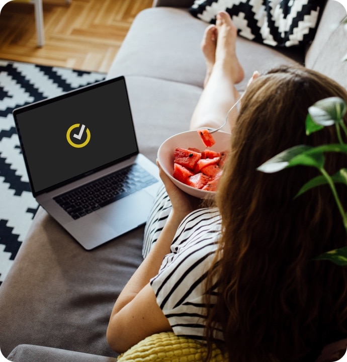 Femme mangeant une pastèque sur un canapé et utilisant un ordinateur portable lançant Norton 360 AntiVirus Plus